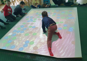 Chłopiec jest na interaktywnej podłodze, na której widnieją kolorowe koła.