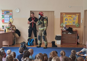 Strażak ubrany do pożaru, prezentuje strój dzieciom.