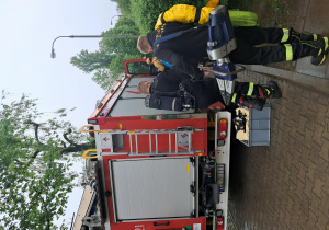 Strażacy pakują sprzęt do wozu strażackiego.