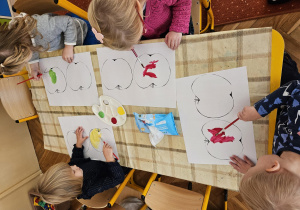 Trzy dziewczynki i jeden chłopiec wypełniają kontury dużych jabłek farbami