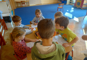 Dzieci siedzą przy stoliku, wykonują prace plastyczne