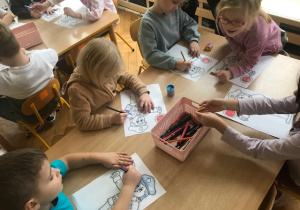 Dzieci kolorują kolorowankę, którą otrzymały od funkcjonariuszki Policji