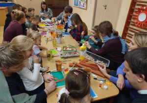 Rodzice z dziećmi wykonują prace plastyczne z papieru kolorowego