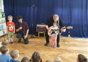 dziewczynka gra na gitarze z pomocą pana