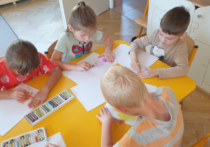 Grupa dzieci przy stoliku dobiera jesienne kolory do swoich prac
