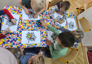 Grupa przy stolikach wykonuje liście, wyklejając je plasteliną