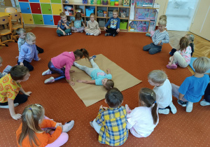 Dzieci siedzą na dywanie podczas zajęć