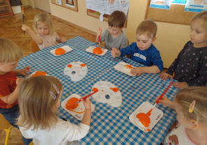 Grupa przy stoliku maluje dynie z masy solnej