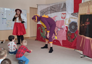 Aktorzy na scenie, za nimi tło z symbolami narodowymi.