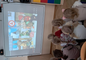 Dzieci siedzą na dywanie i oglądają prezentację