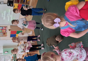 Dzieci stoją na dywanie i bawią się swoimi misiami