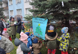 Dzieci wieszają plakat na choince.