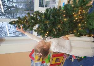 Dziewczynka wiesza pierwszą bombkę na choince.