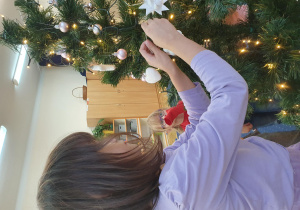 Dziewczynka wiesza śnieżynkę na choince.