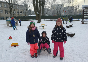Dzieci pozują do zdjęcia na śniegu, dziewcznka siedzi na sankach.