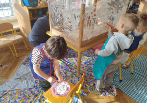 Chłopiec rozrabia białą farbę w miseczce