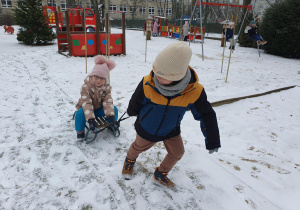 Chłopiec ciągnie dziewczynkę na sankach