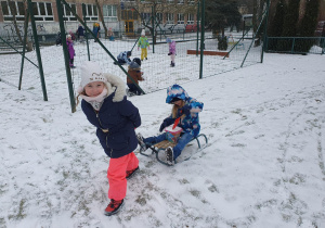 dziewzynka ciągnie koleżankę na sankach