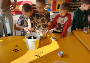 Chłopcy nakładają ziemię do pomalowanych doniczek