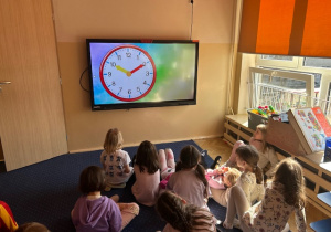 Dzieci oglądają film edukacyjny pt. "Nauka zegara dla dzieci - wytłumaczenie oraz ćwiczenia"