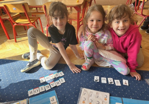 Dziewczynki korzystając z albumu liter i cyfr układają wyrazy