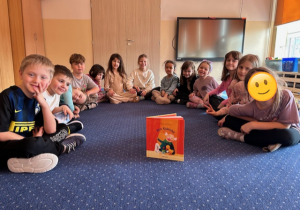 Dzieci siedzą na dywanie pozując do zdjęcia z konkursową książką Wojciecha Widłaka "Pan Kuleczka"