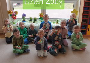 Grupa dzieci prezentuje wykonane żabki na tle dekoracji okiennej