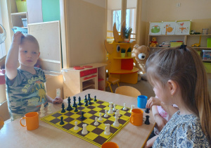 Chłopiec drapie się po głowie siedząc przy szachownicy