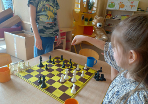 Dziewczynka unosi rękę nad szachami.