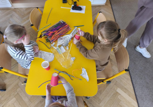 Dziewczynki ozdabiają papierowe kubeczki kolorowymi drucikami