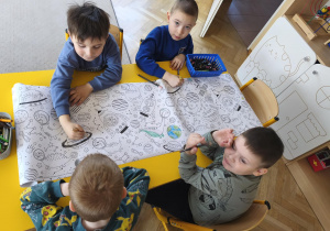 Chłopcy kolorują papier z motywami planet, rakiet i kosmonautów