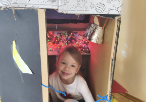 Dziewczynka siedzi przed rakietą wykonaną przez grupę