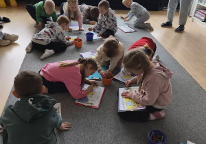 Grupa dzieci koloruje rysunki na dywanie