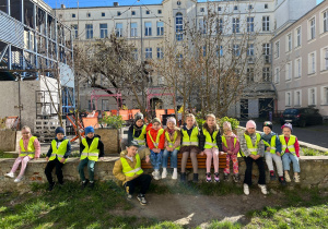 Grupa siedzi na murku przed budynkiem