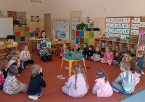 Dzieci siedzą w kole i słuchają Pani