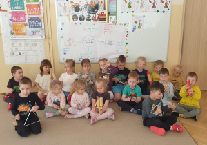 Grupa dzieci siedzi na dywanie i gra na instrumentach
