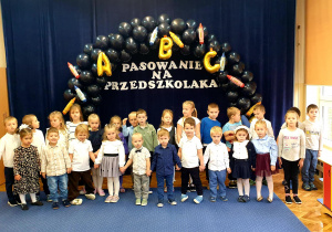 Grupa dzieci w wieku od 3 do 6 lat na tle granatowej dekoracji "Pasowanie na Przedszkolaka"