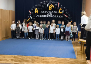 Grupa dzieci na tle napisu, z prawej strony nauczycielki