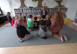 Grupa siedzi w sali bibliotecznej i słucha opowiadania