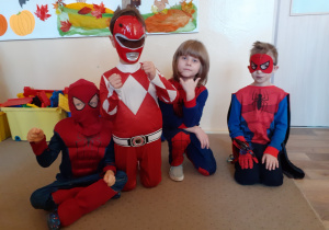 Na dywanie siedzi czterech chłopców przebranych za superbohaterów.