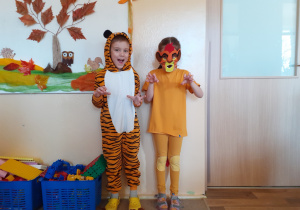 Na tle ściany stoi chłopiec w stroju tygrysa i dziewczynka przebrana za lwa.