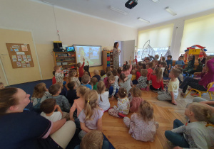 Nauczycielka pokazuje dzieciom obrazek, dzieci siedzą na dywanie.