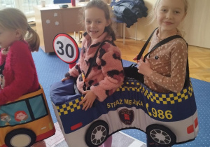 Dziewczynki przebrane za pojazd Straży Miejskiej uśmiechają się do zdjęcia.