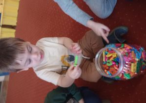 Chłopiec wybiera plastikową literę z wielkiego słoika.