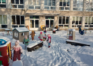 Dzieci ubrane w stroje zimowe zwiedzają ogród przedszkolny.