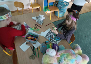 Dzieci przy stoliku kolorują obrazki.