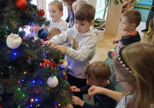 Dzieci wspólnie dekorują drzewko.