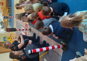 Strażnicy miejscy prowadzą pogadankę z dziećmi siedzącymi na dywanie.